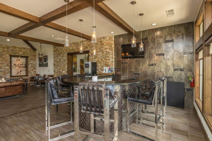A bar with chrome stools and a brick backdrop. Includes hanging lights, TV, and wooden beams.
