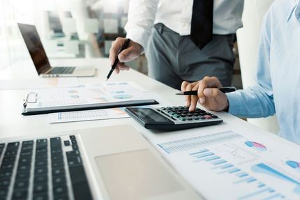 A Man is Using a Calculator While Another Man Stands Behind Him — Ardent Office Equipment in Hermit Park, QLD