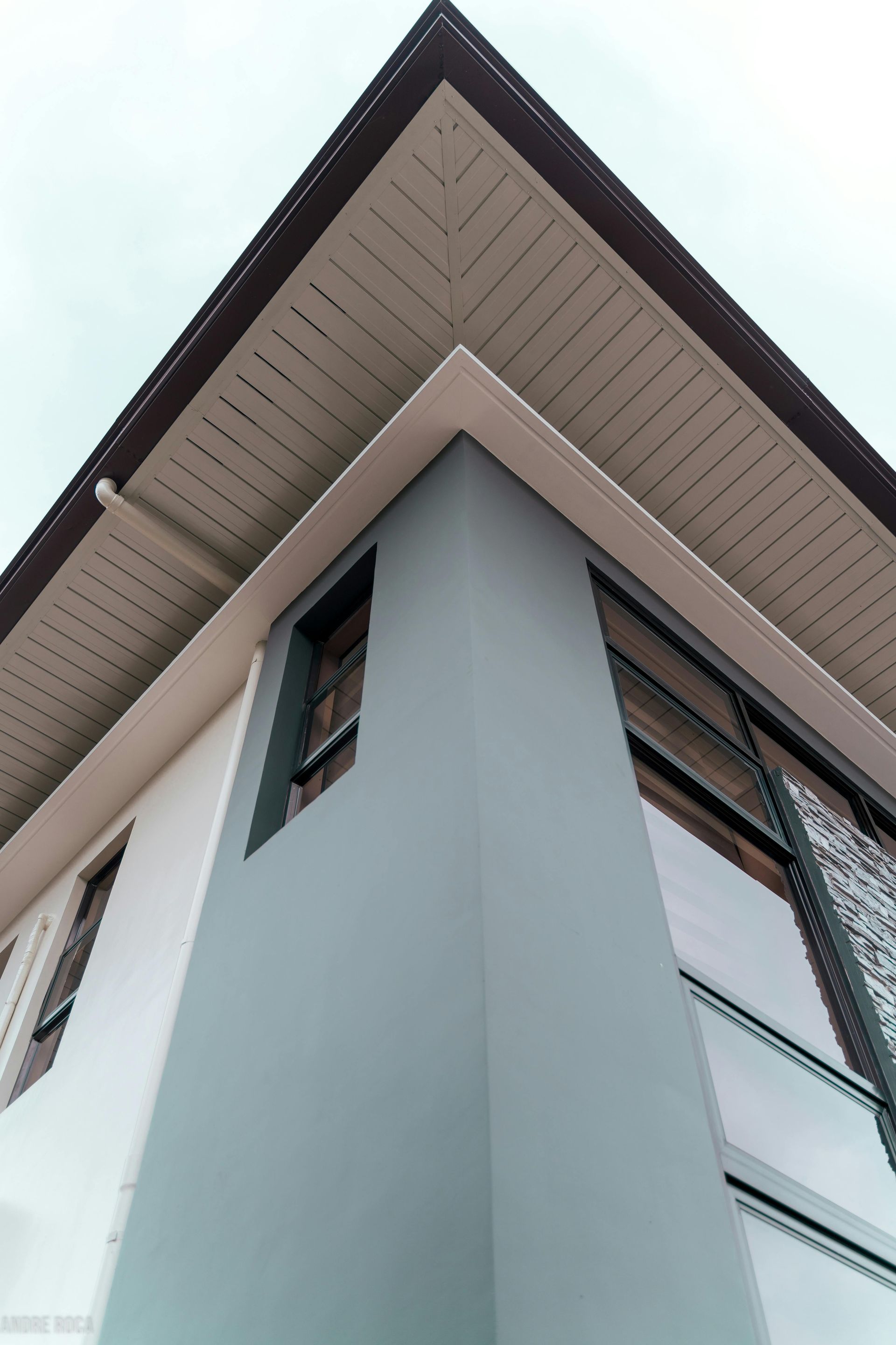 Modern building corner with light gray walls and dark wood roof soffit, viewed from below