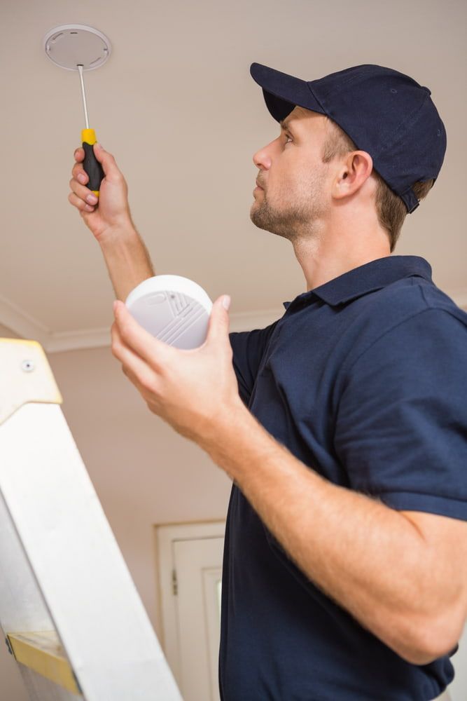 Handyman Installing Smoke Detector With Screwdriver On The Ceiling — Premium Electrical Solutions in Bundaberg, QLD