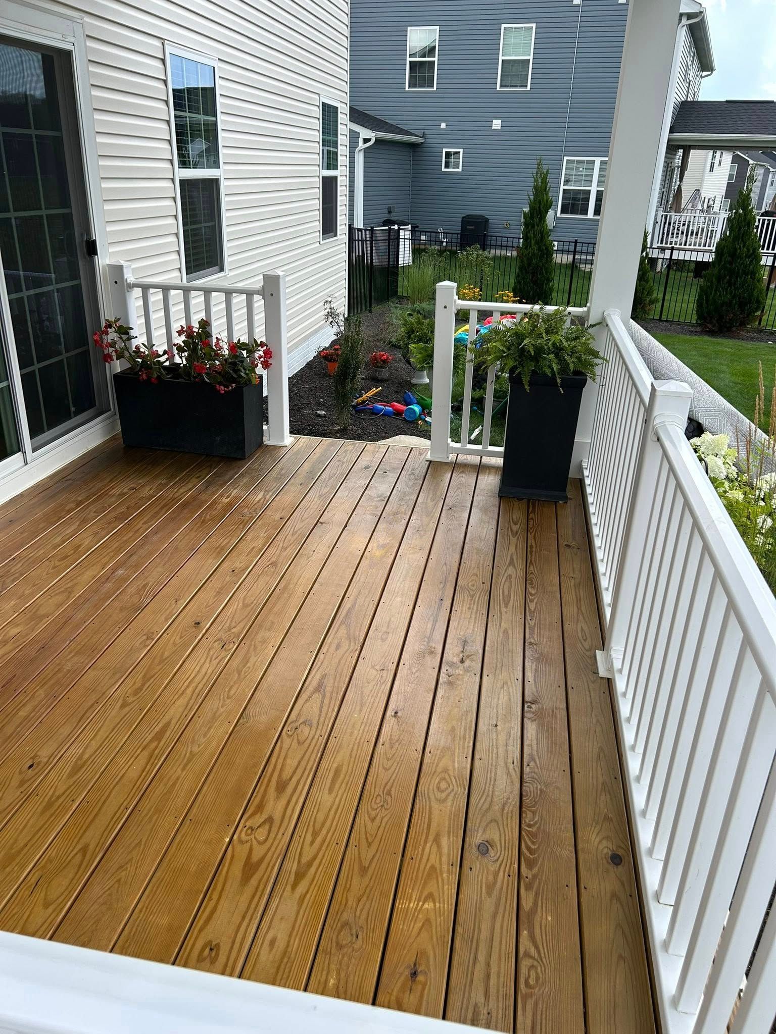 Wooden deck with white railing, potted plants, and a view of a backyard.