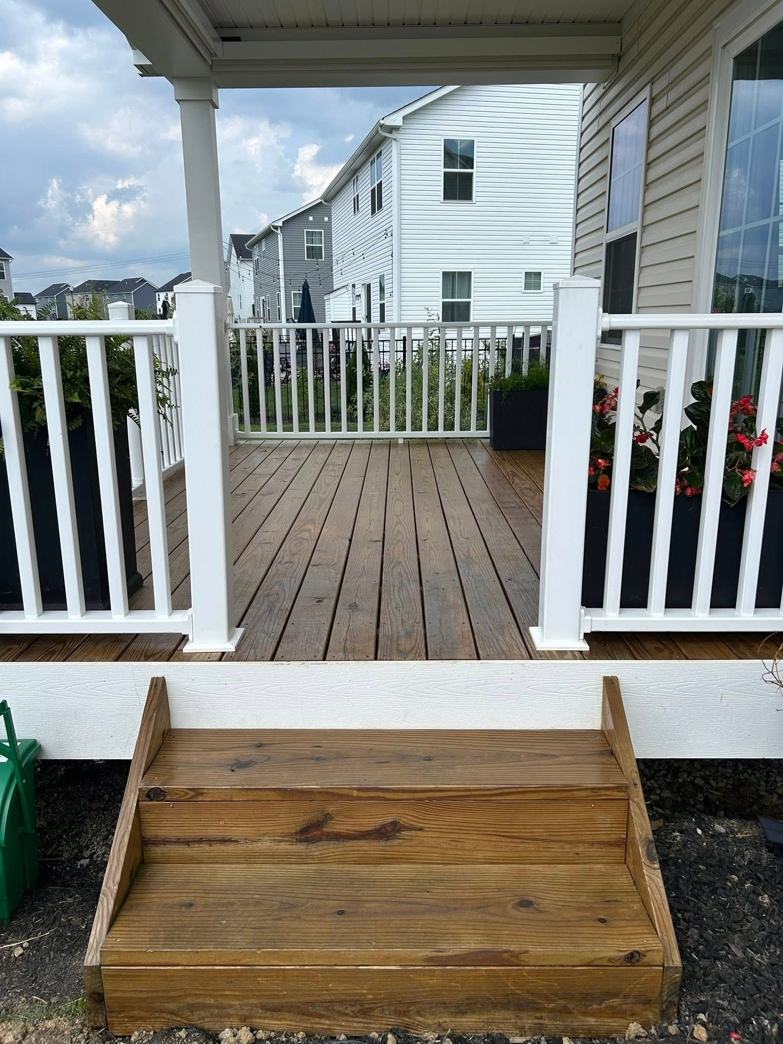 Wooden deck with white railing, steps leading up to it, and a partially visible building in the background.