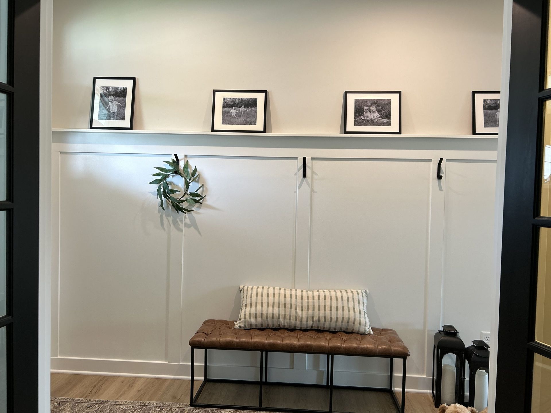 Entryway with white paneled walls, bench, wreath, and framed photos.