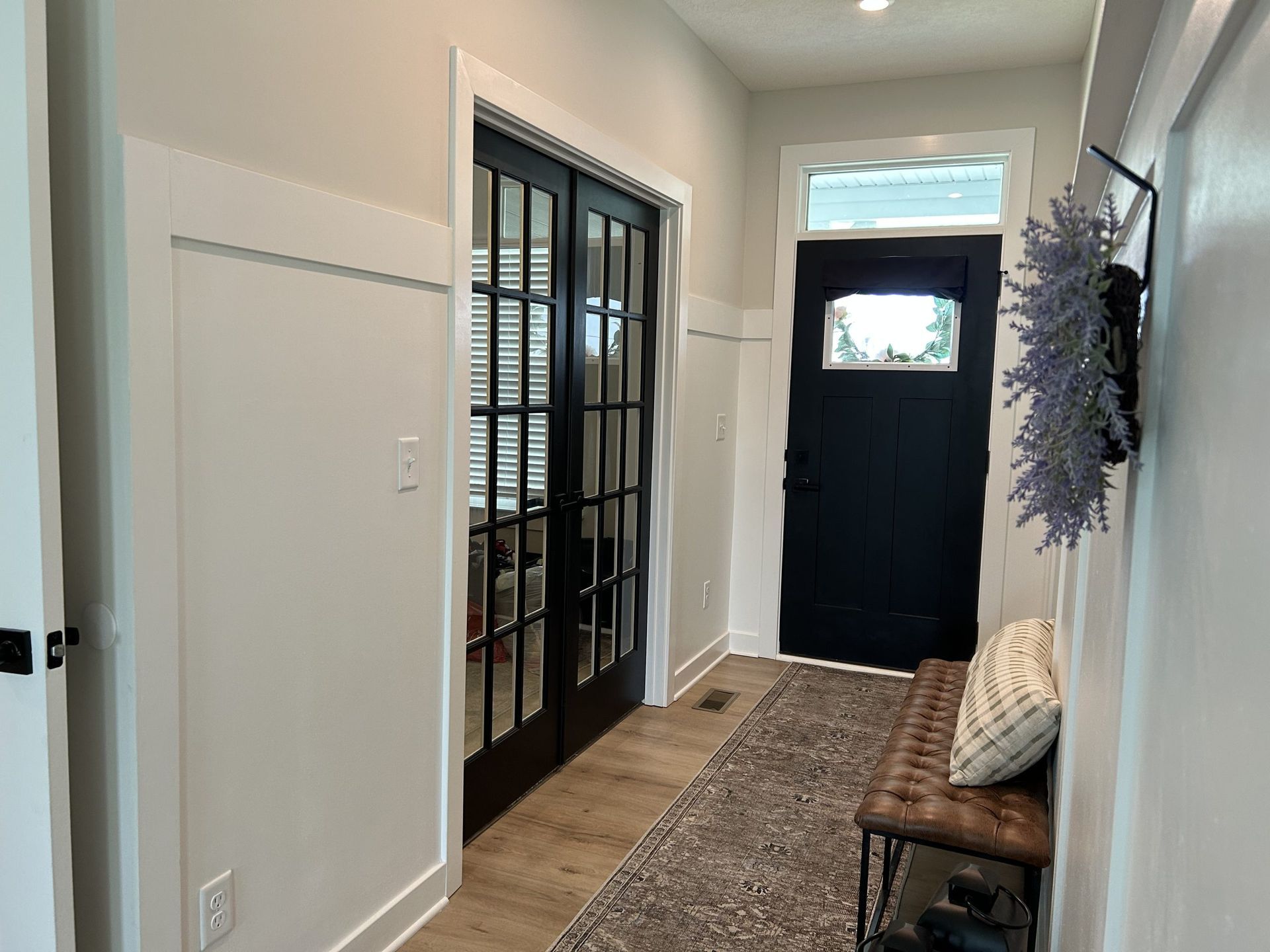 Hallway with black doors, wainscoting, rug, bench, and a wreath on the wall.