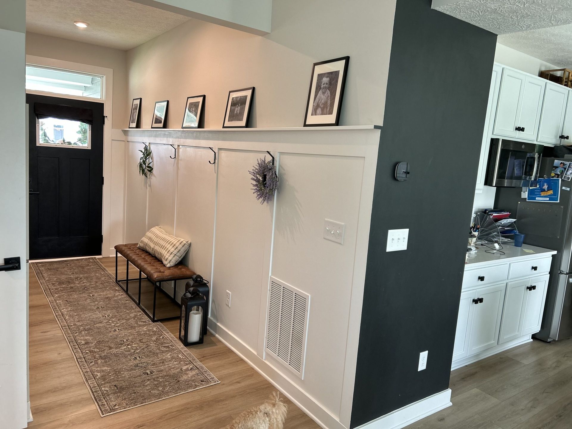 Entryway with black door, wooden bench, beige wall, and dark accent wall.