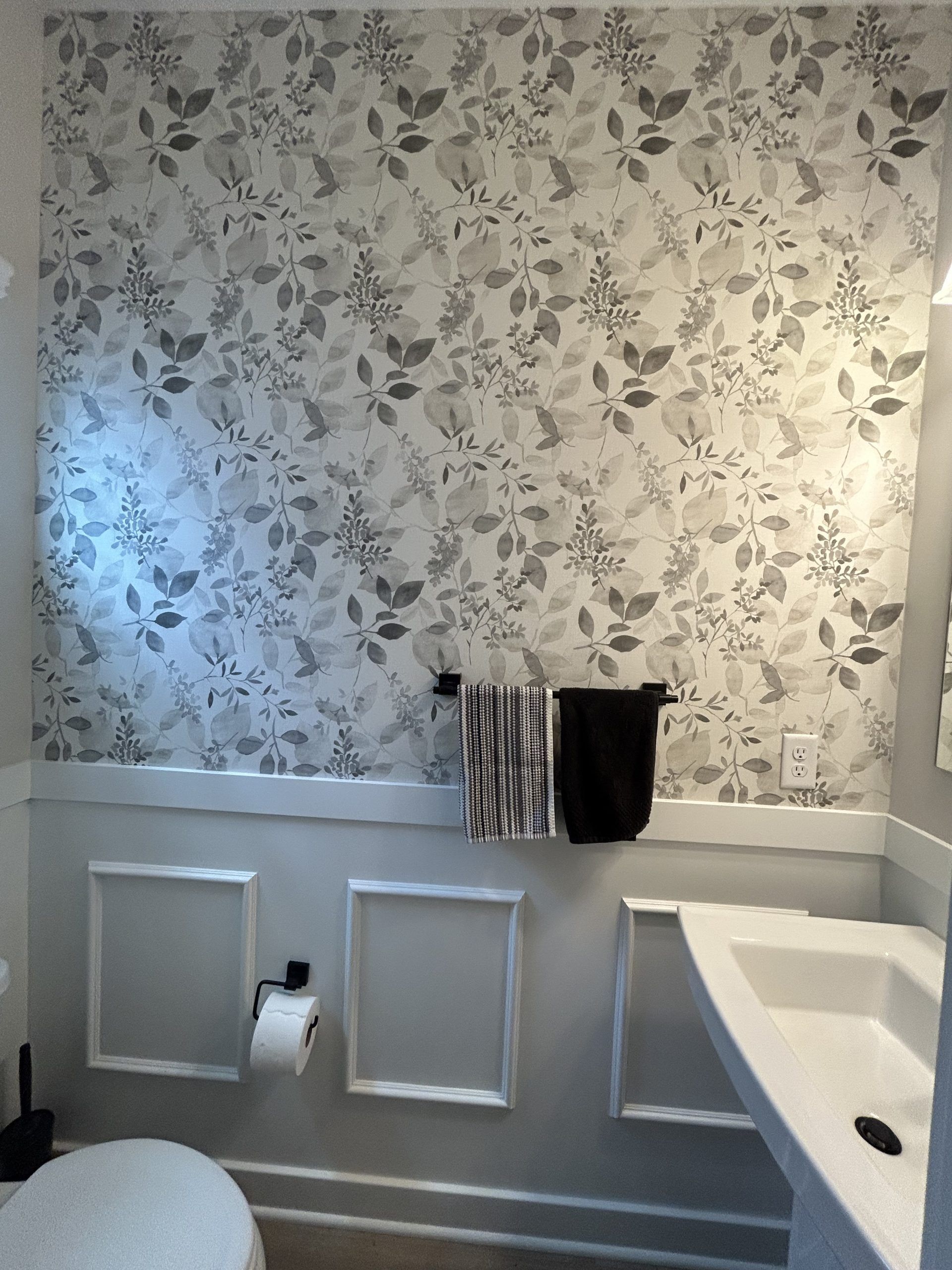 Powder room with floral wallpaper, white wainscoting, and a white sink.