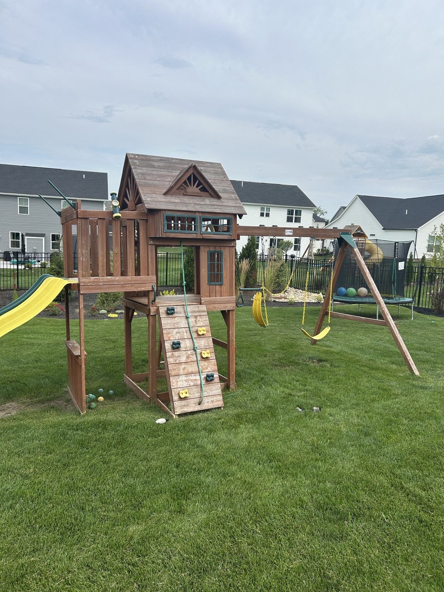 Wooden playset with a slide, climbing wall, and swing set in a grassy backyard.