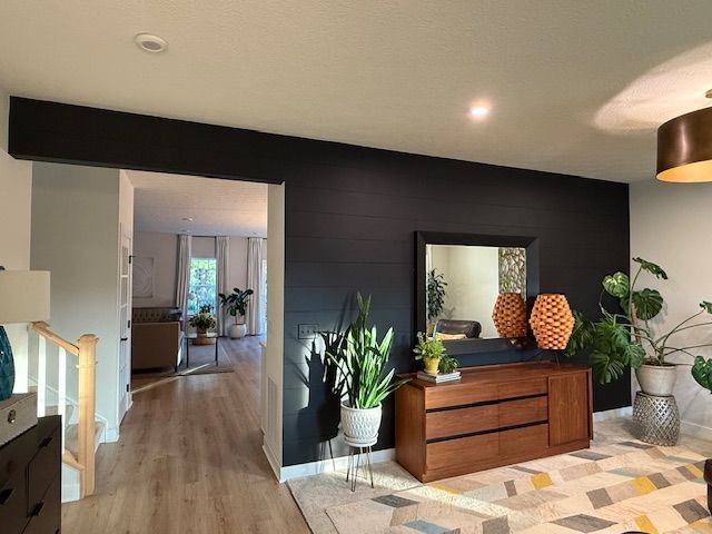 Living room with dark accent wall, wooden dresser, plants, and doorway to another room.