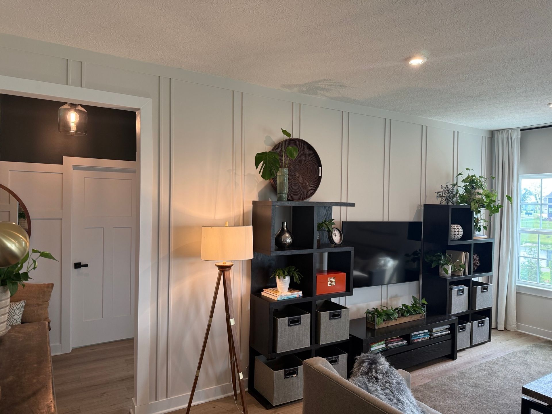 Living room with a wood floor lamp, shelves, a TV, and a panelled wall.