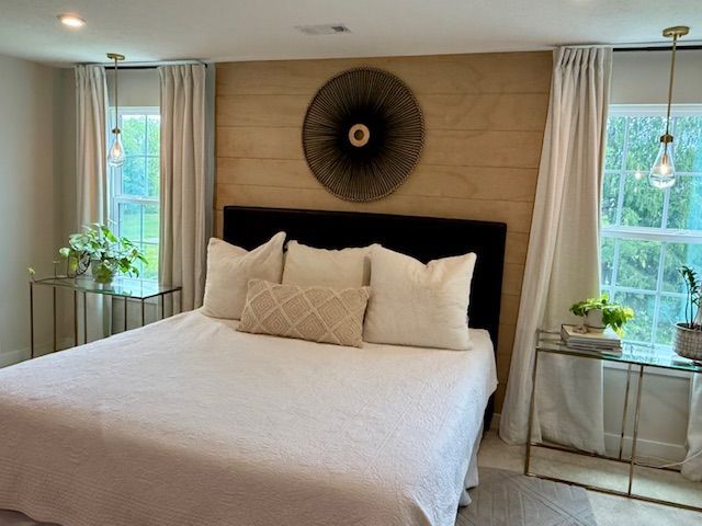 Bedroom with a bed, nightstands, windows with curtains, and decorative wall art.