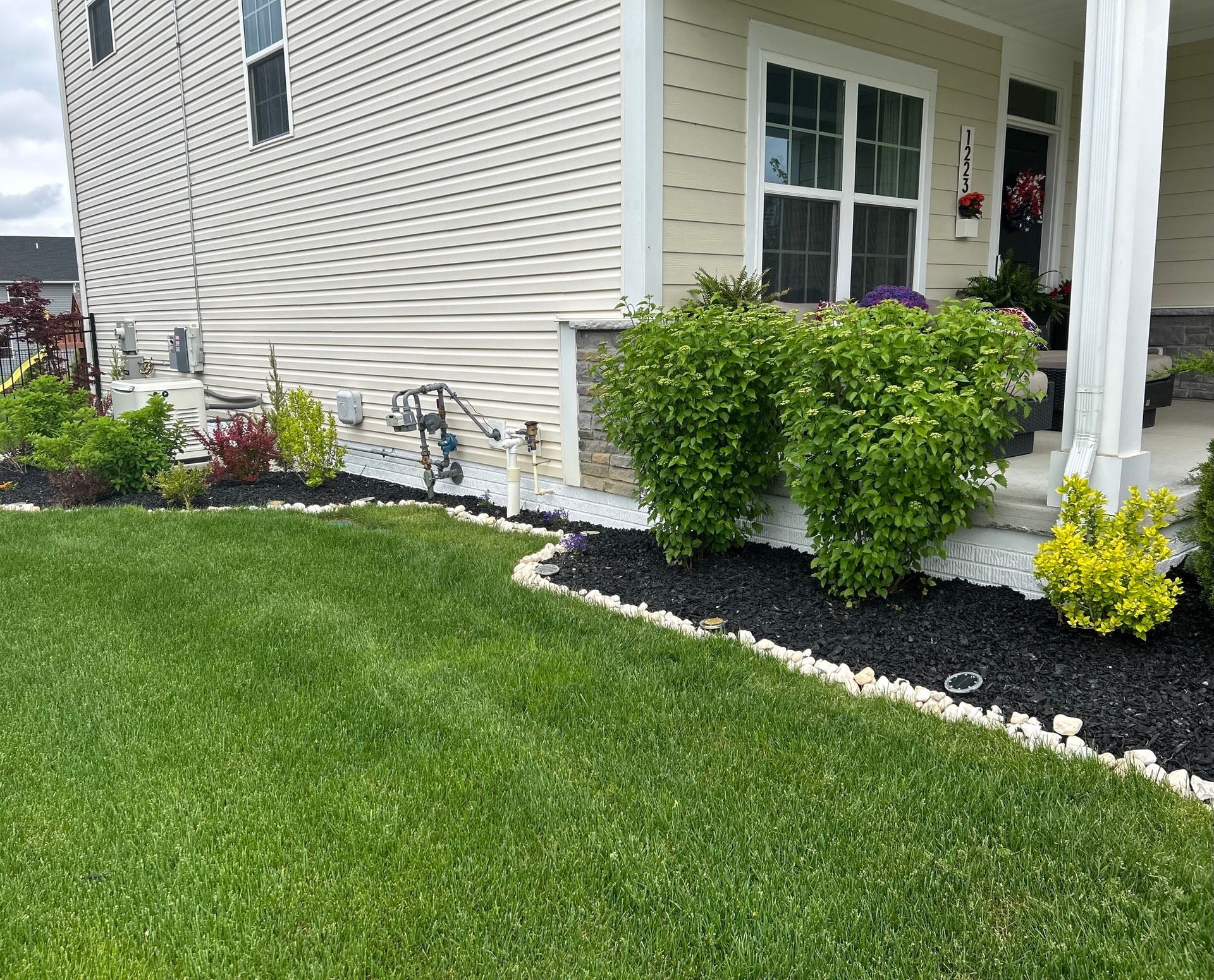 Green lawn borders a house with black mulch, plants, and white edging.