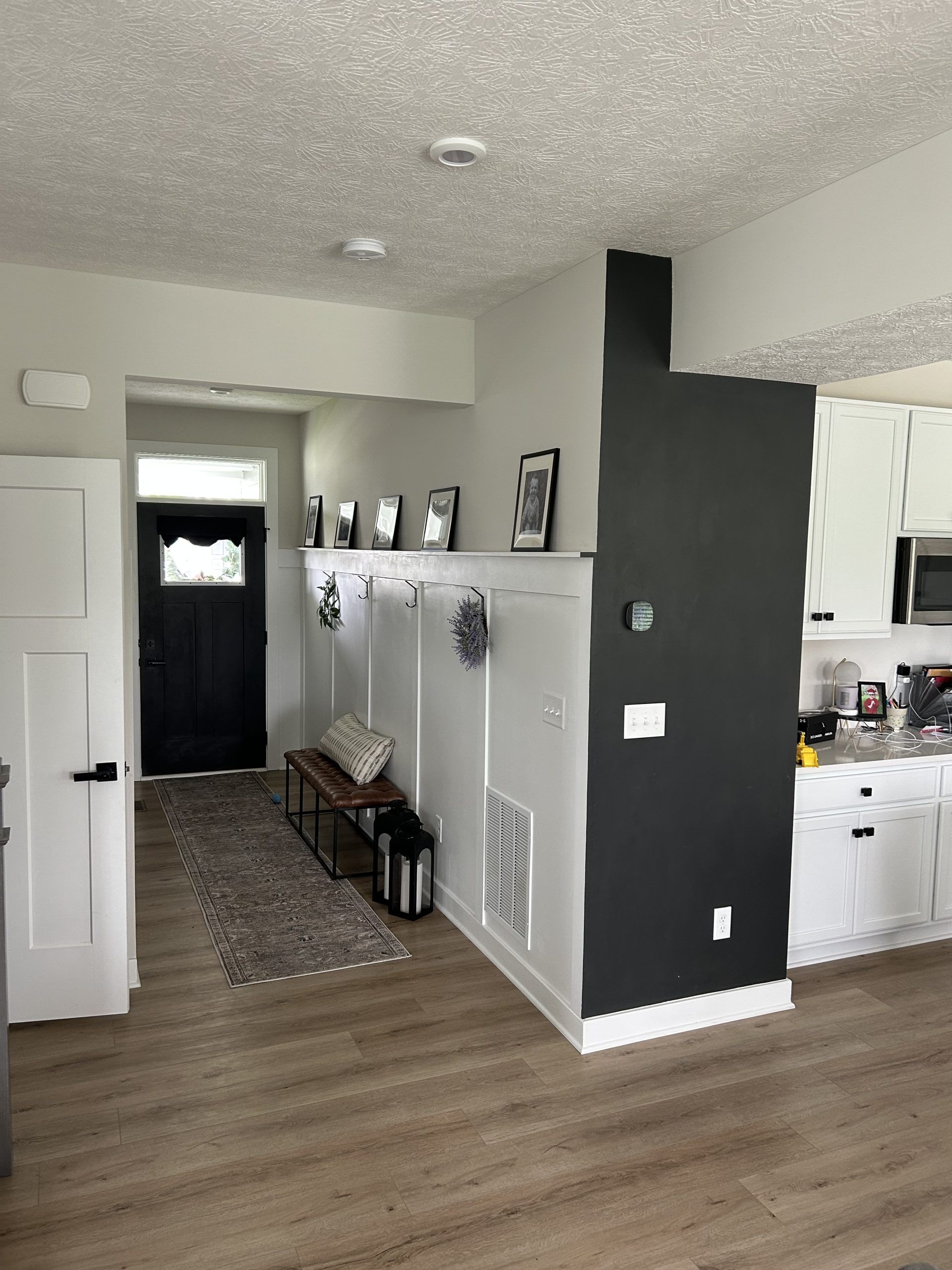 Entryway with black door, white and black walls, bench, hooks, and a dark grey accent wall.