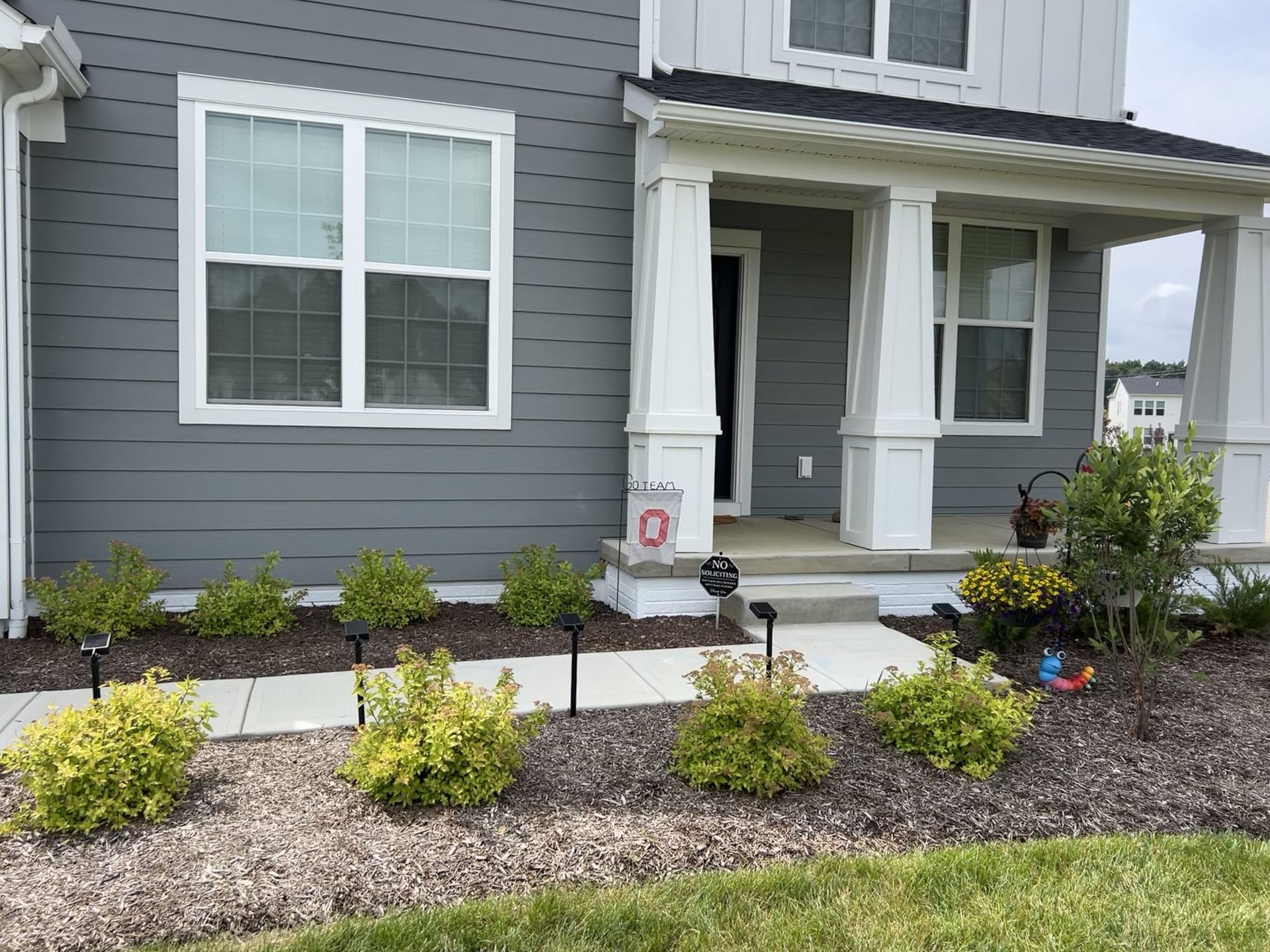Gray house with white trim, front porch, and small yellow-green bushes lining the walkway.
