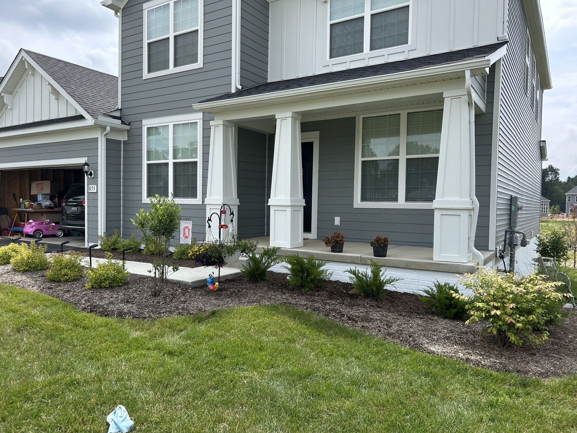 Gray house with a white porch and dark mulch landscaping.
