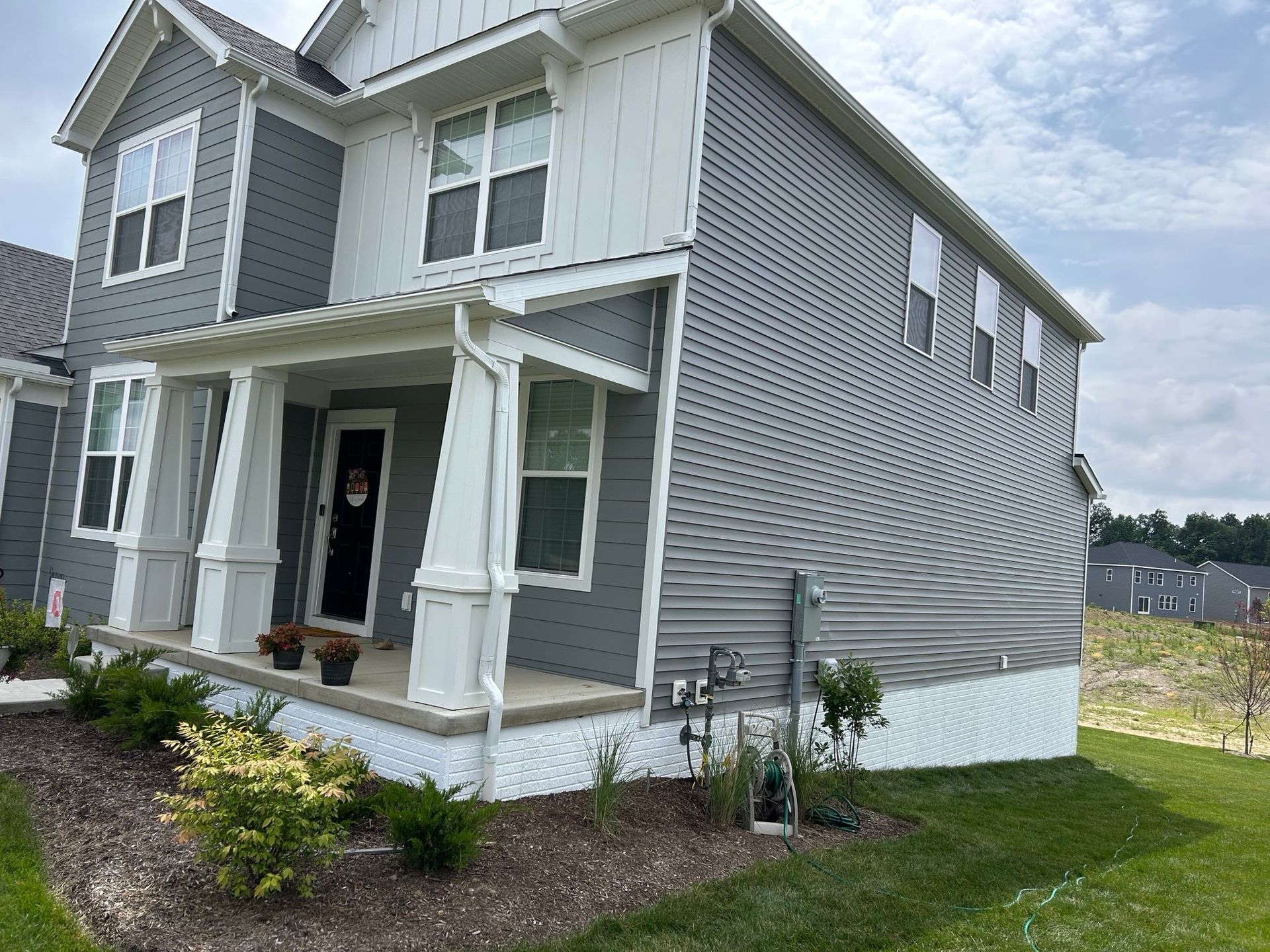 Two-story house with gray siding and white trim, porch, and a grassy yard under a cloudy sky.