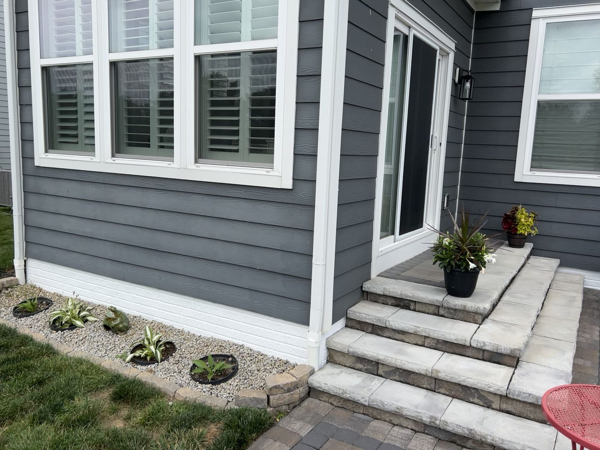 Exterior view of a house with gray siding, white trim, and stone steps leading to a sliding glass door.