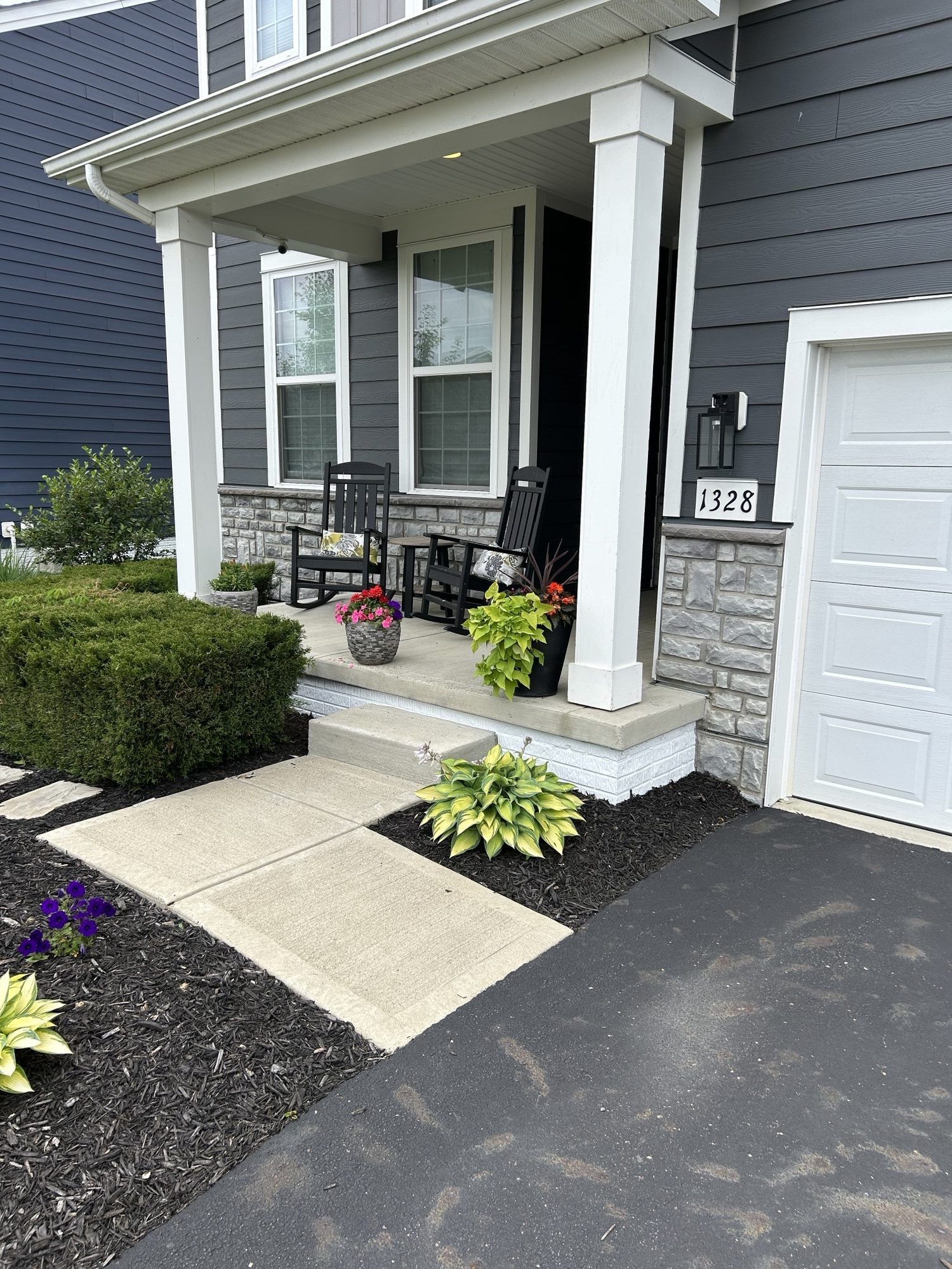 Gray house with a small porch, black rocking chairs, and landscaped front yard.