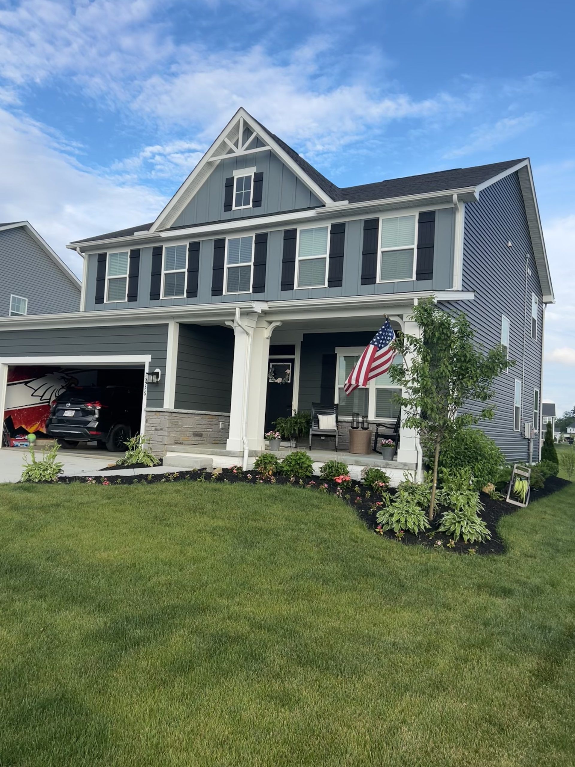 Two-story gray house with a porch, garage, and American flag under a blue sky.