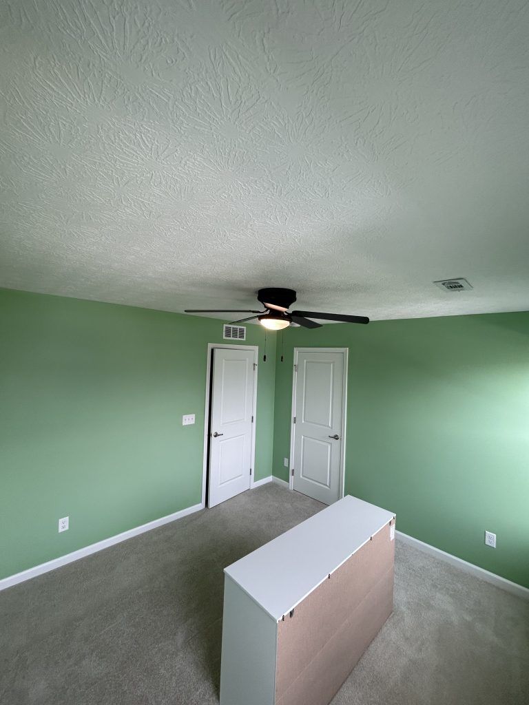 Green-walled bedroom with two white doors, a white dresser, and a ceiling fan.