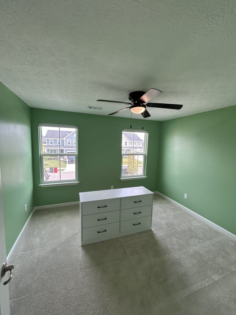 Bedroom with green walls, white dresser, two windows, and a ceiling fan.