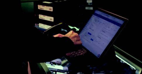 Person typing on a laptop in a dark setting, possibly a control room. The screen displays a user interface.