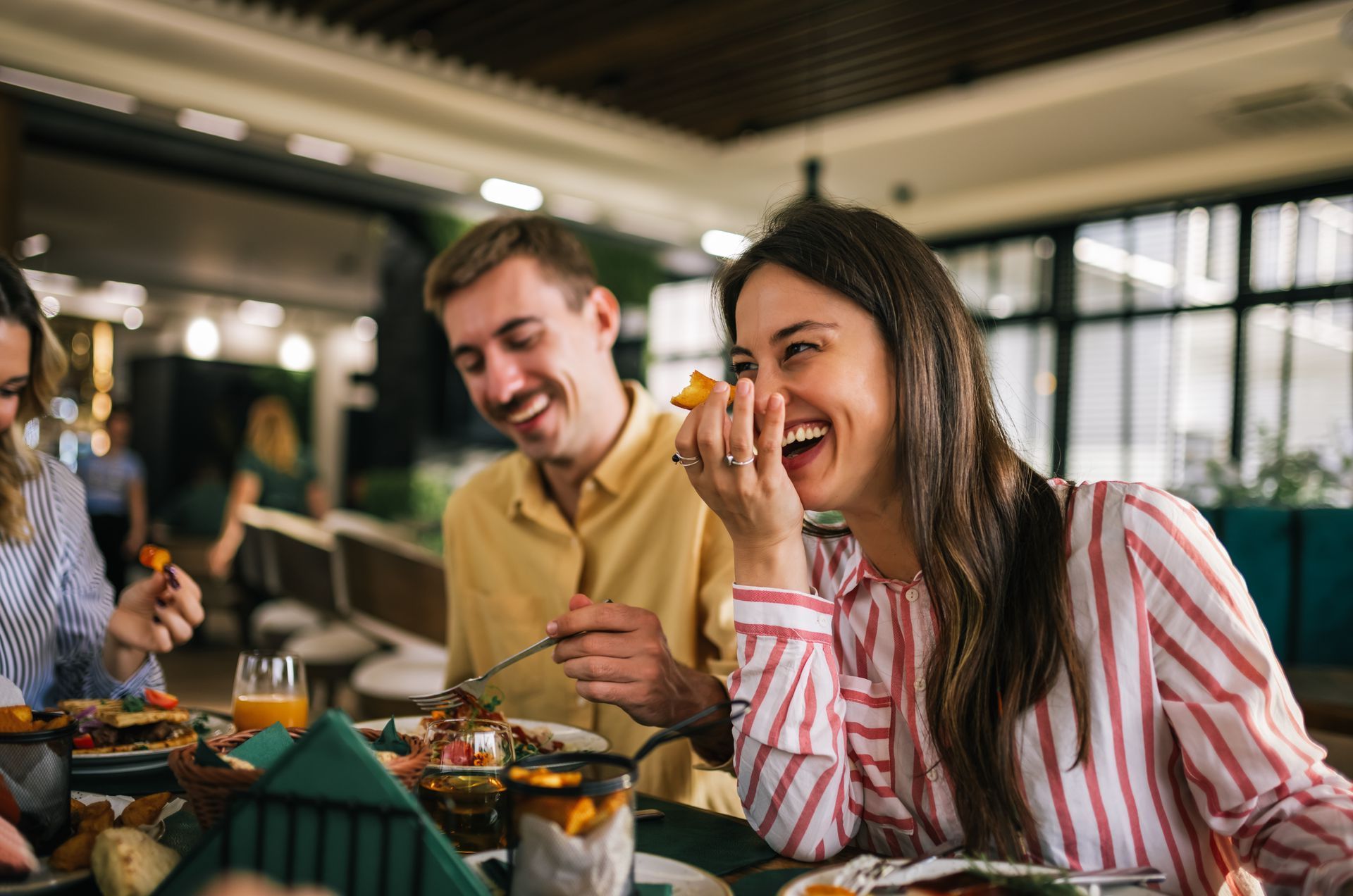 People laughing around a table in a restaurant, enjoying food.