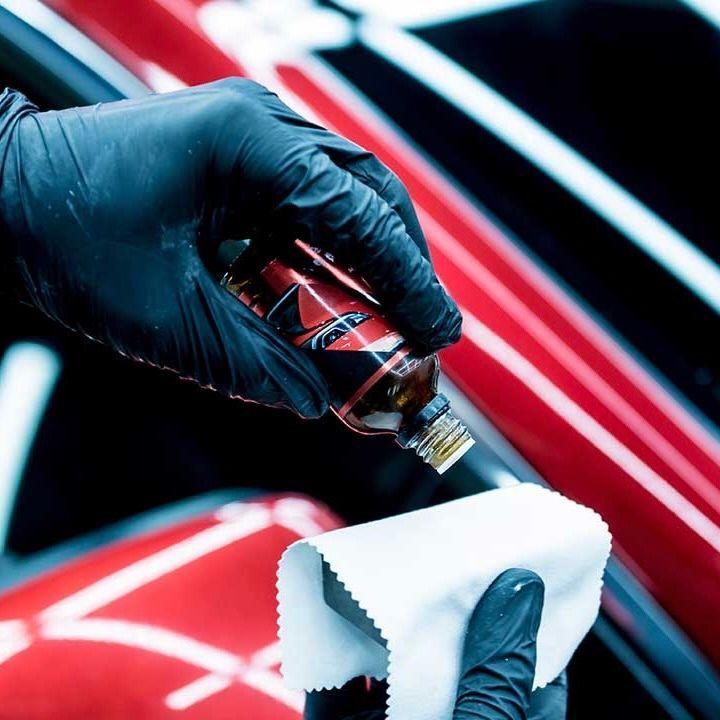 Person in black gloves applying ceramic coating to a red car with a white cloth.