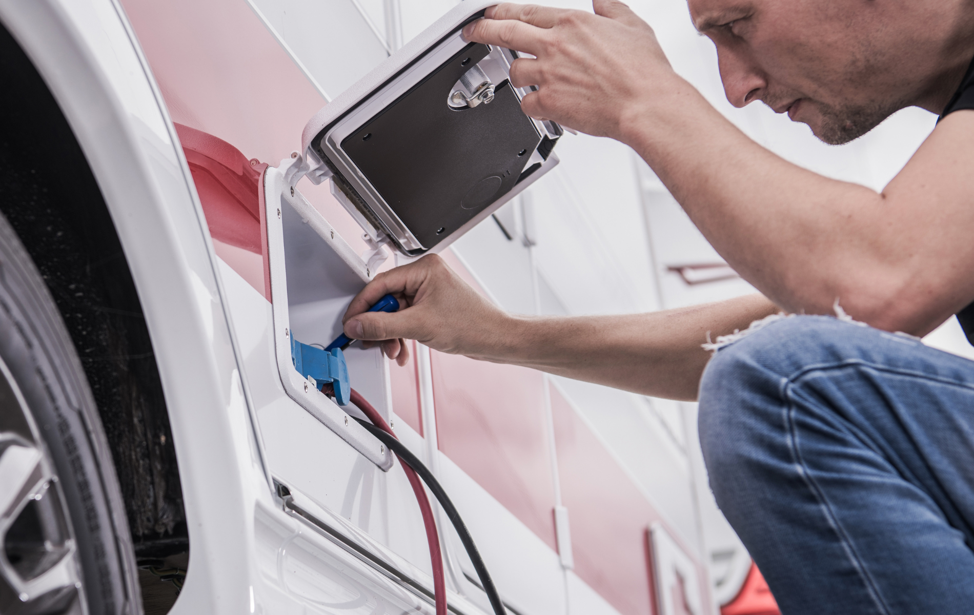 Man plugging an electrical cable into a motorhome’s side. He’s kneeling down, focusing.