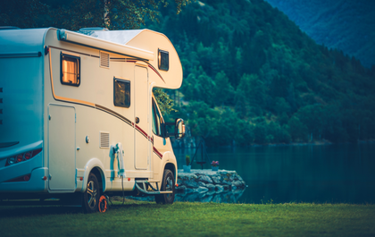 A rv is parked next to a lake with mountains in the background.