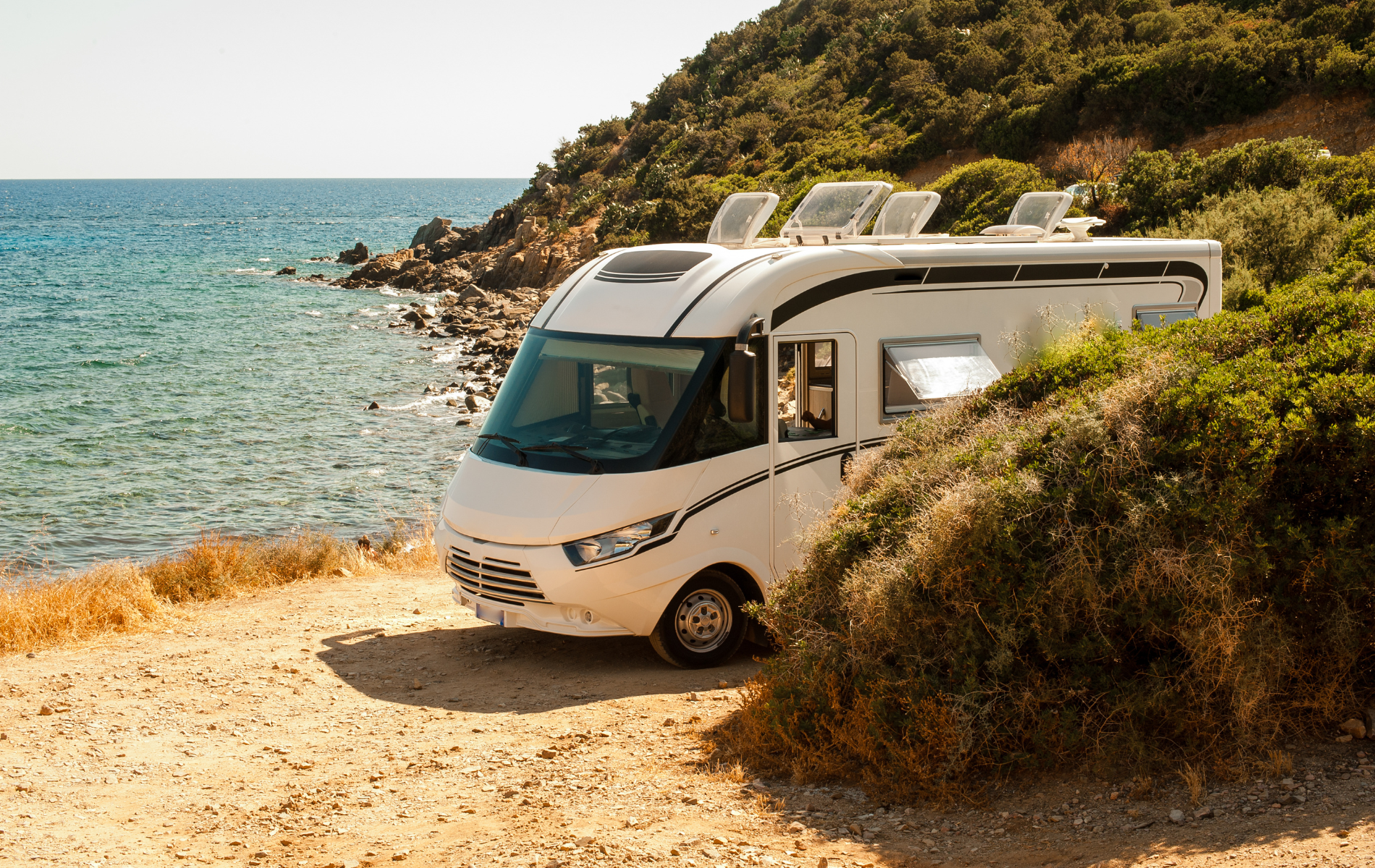 A white rv is parked on the beach next to the ocean.