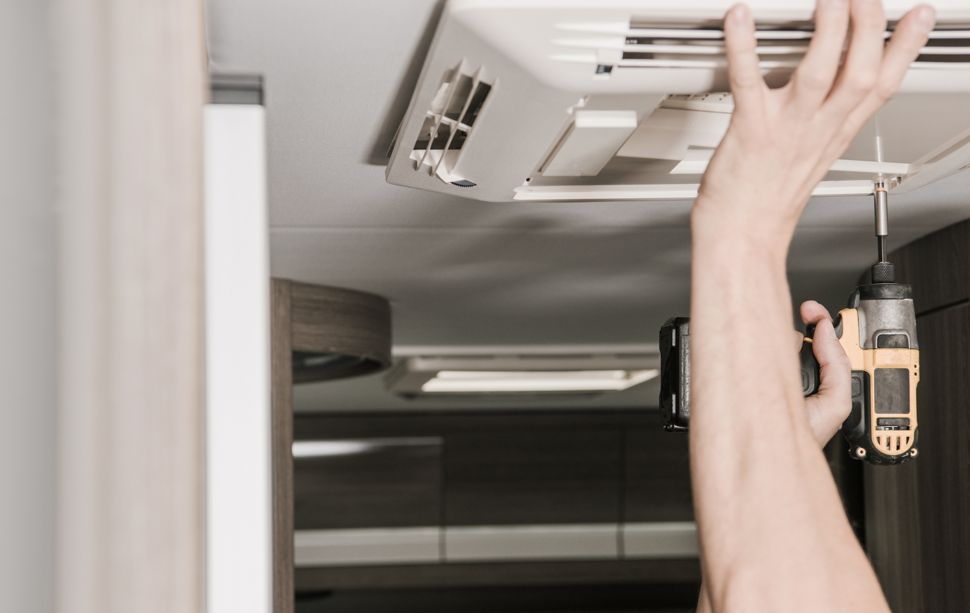 A person is fixing a ceiling fan with a drill.