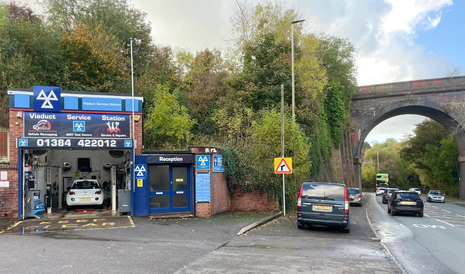 A car is parked in front of a garage next to a bridge.