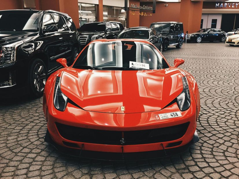 Red Ferrari sports car parked in a showroom with other luxury vehicles.