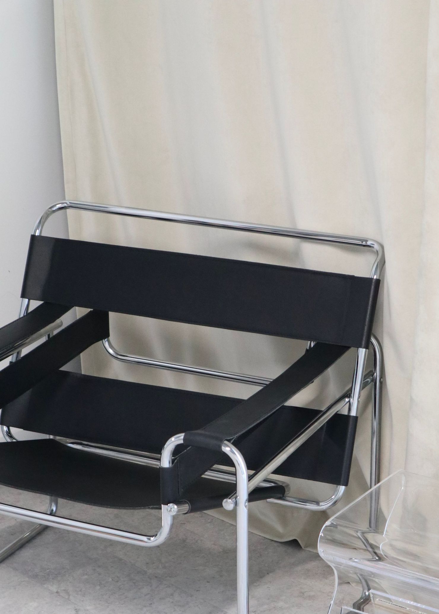 A black chair is sitting in front of a white curtain