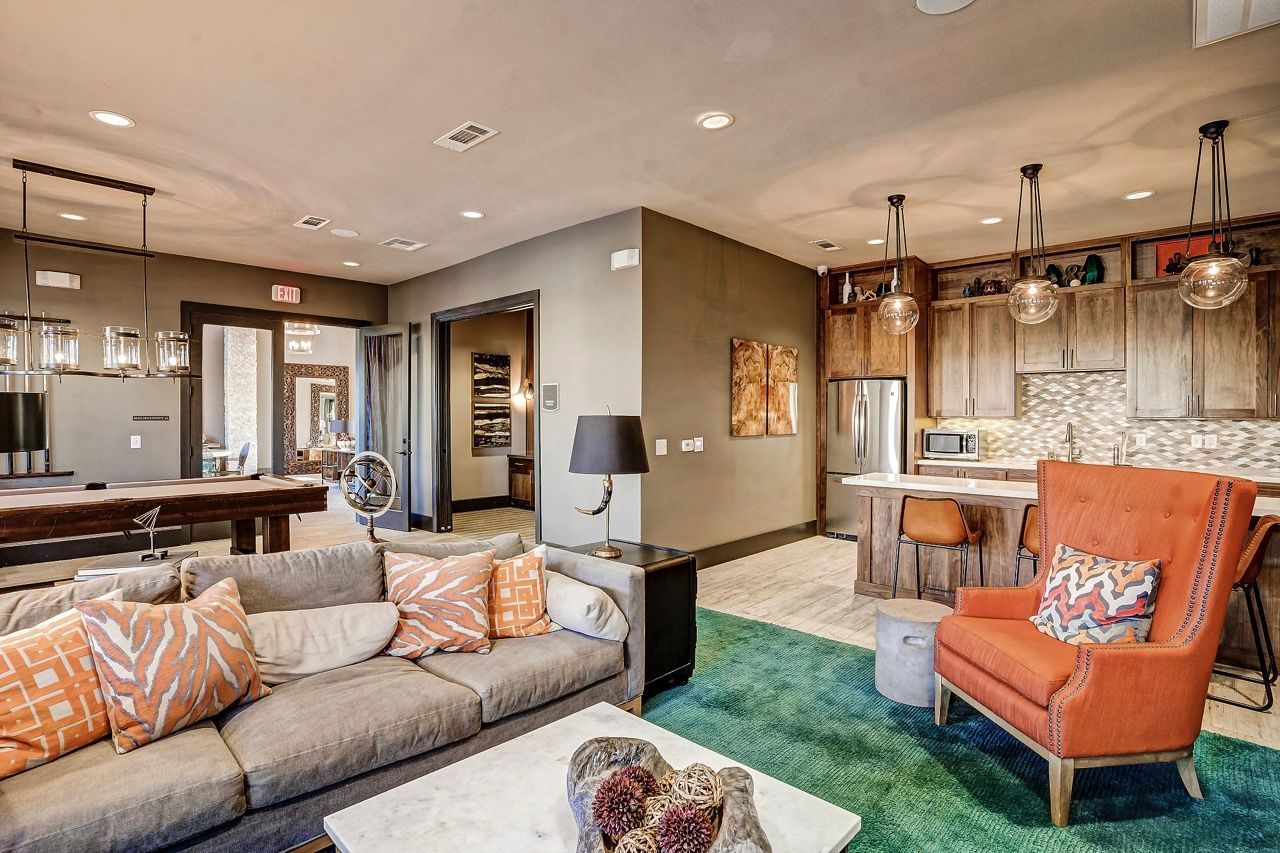 Open-concept community lounge with a sofa, orange armchairs, and a kitchen bar.