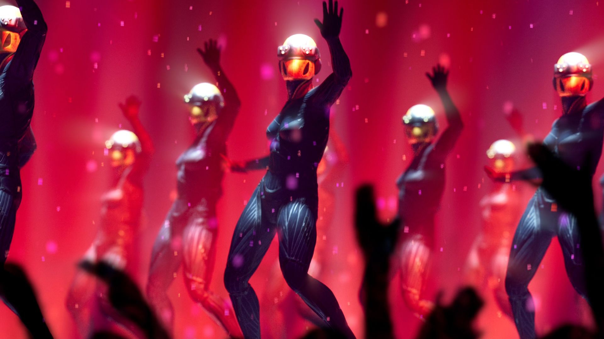 Woman dressed in cyber costumes dance on stage with pink stage lights shining down on them