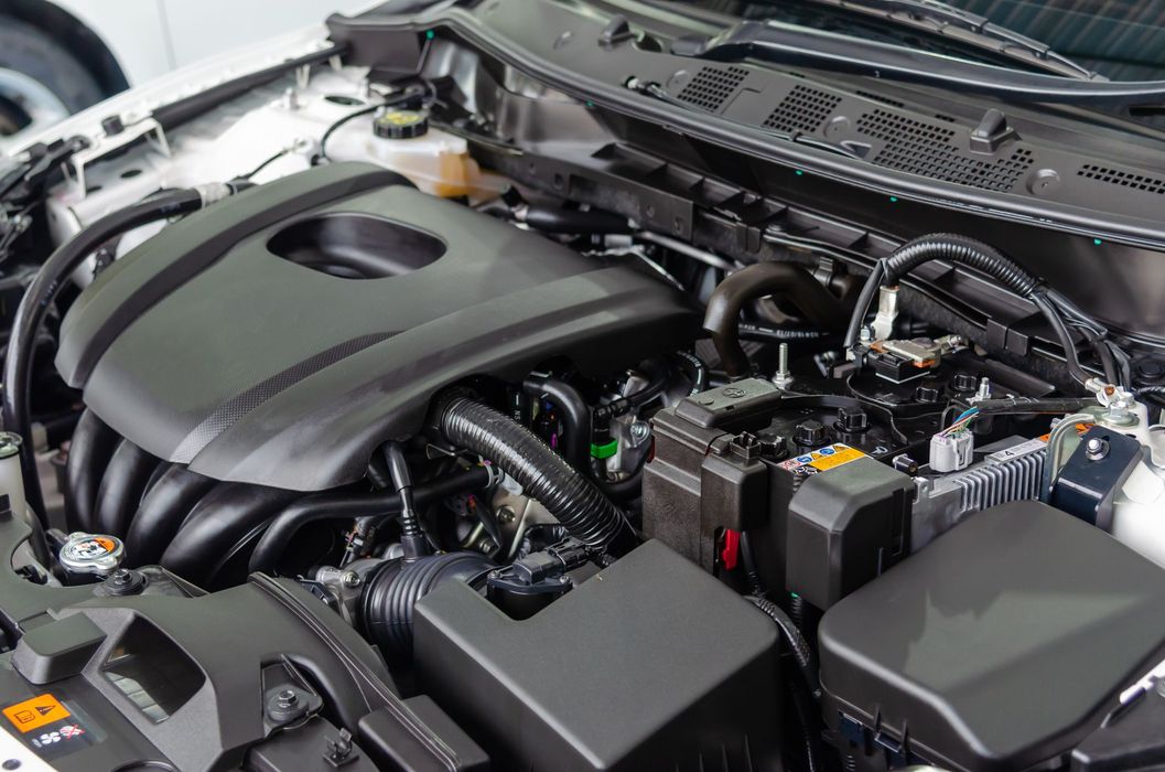 A top-down view of a clean car engine bay with black plastic covers, hoses, and mechanical components.