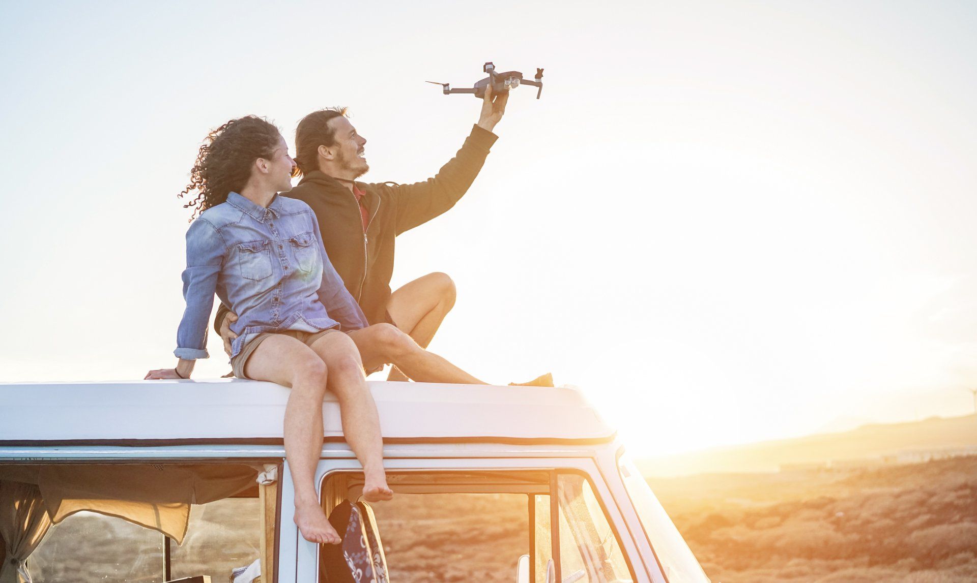 Happy Couple Using A Drone Sitting On Top Of Vintage Minivan — Phoenix, AZ — Apartment & Home Solutions
