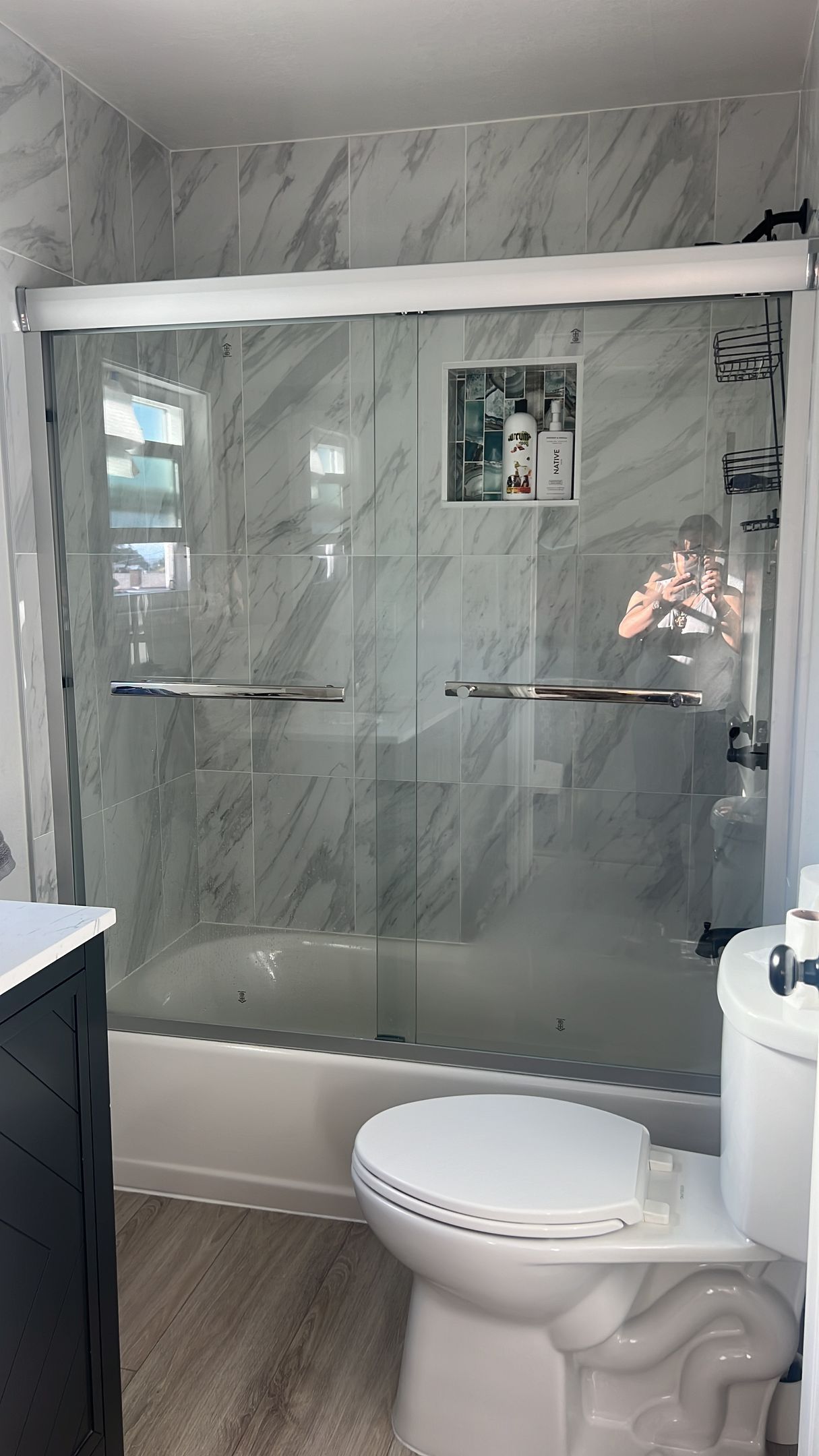 Bathroom with marble-look shower and glass doors, toilet in front, and sink to the left.