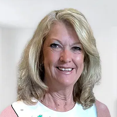 Woman with blonde hair smiling, wearing a patterned top, in a well-lit space.