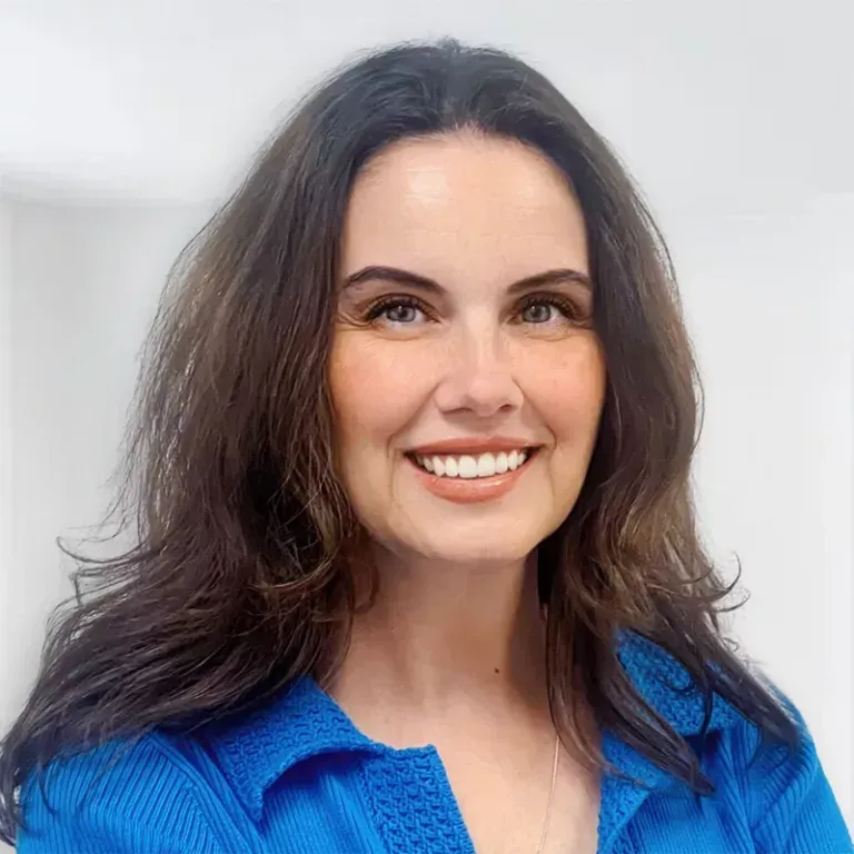 Woman with long dark hair smiles, wearing a blue collared sweater.