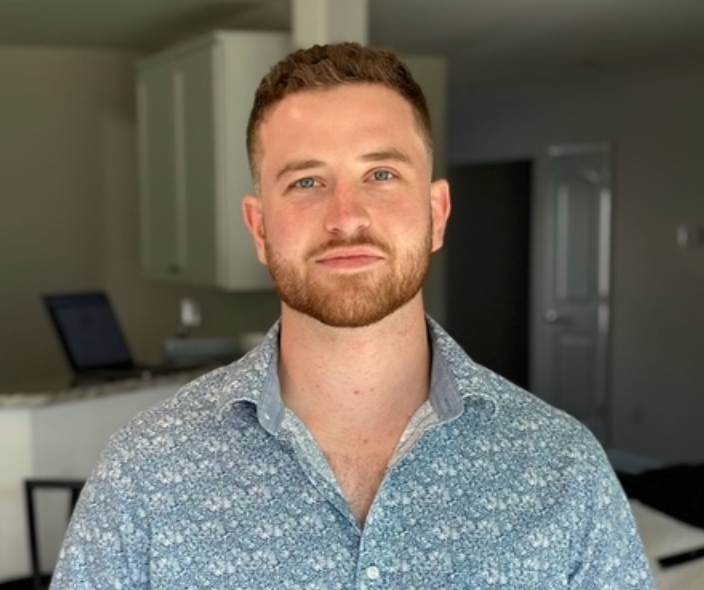 A man with a beard is wearing a blue shirt and standing in a room.