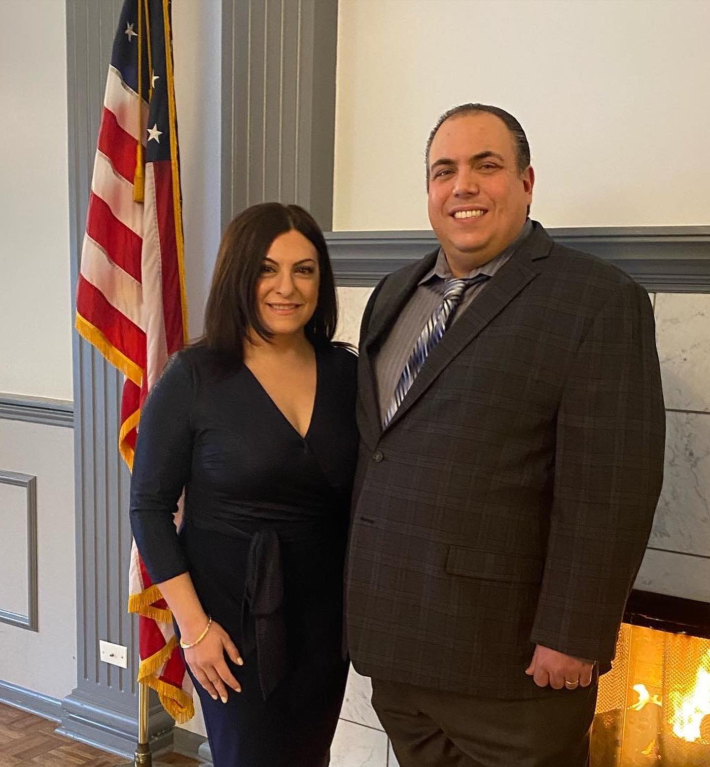 A man and a woman are posing for a picture in front of an american flag.