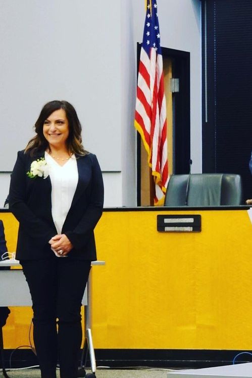 A woman in a suit stands in front of an american flag