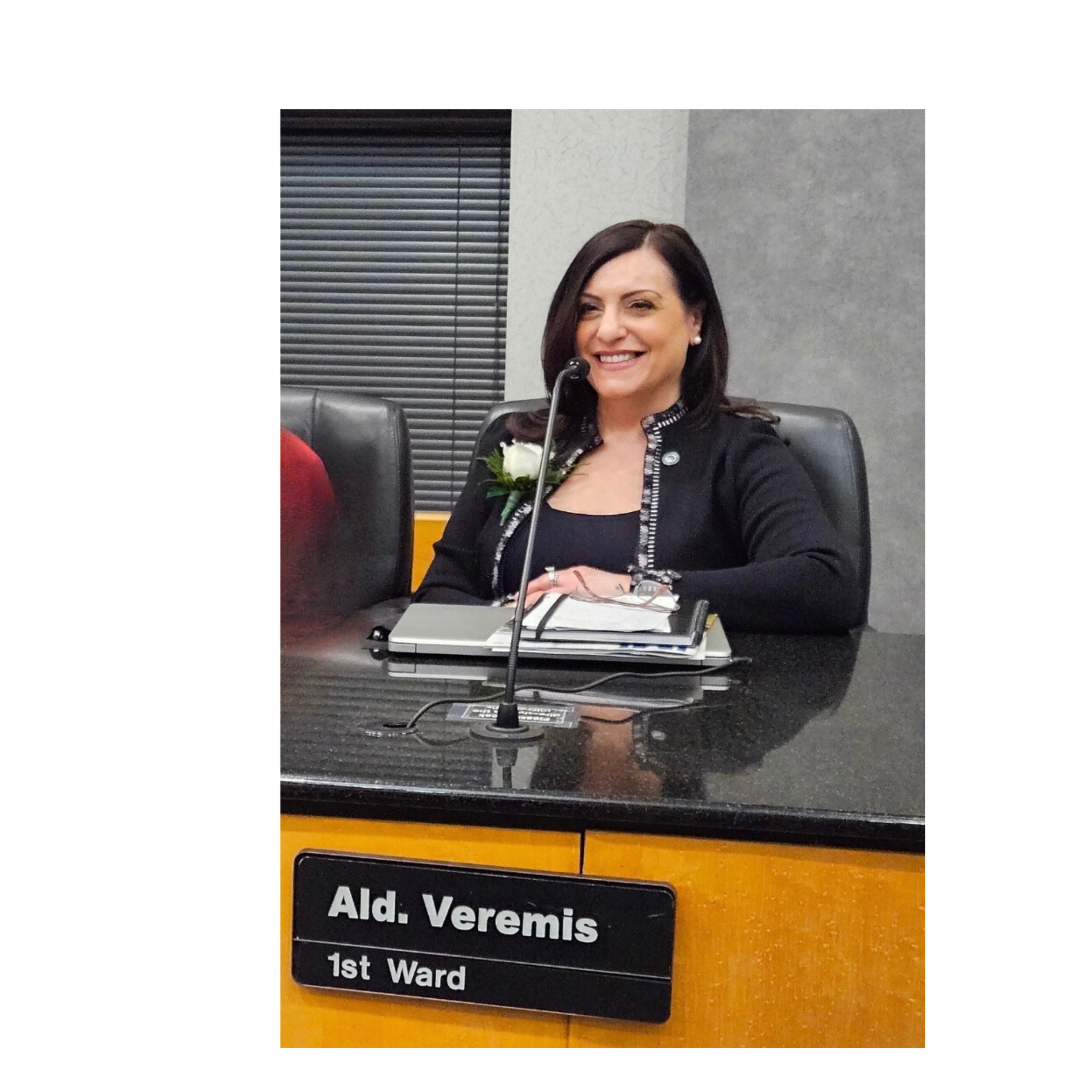 A woman is sitting at a desk with a sign that says aid veromis 1st ward