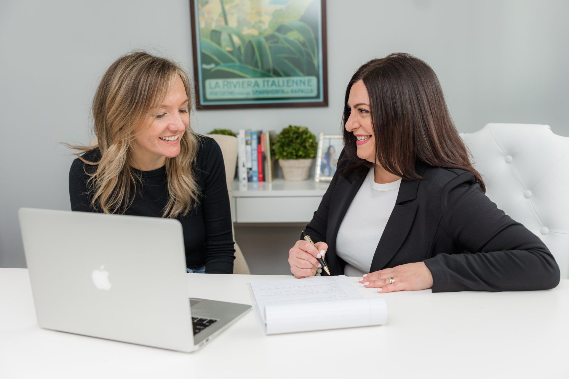 Two women are sitting at a desk with a laptop.