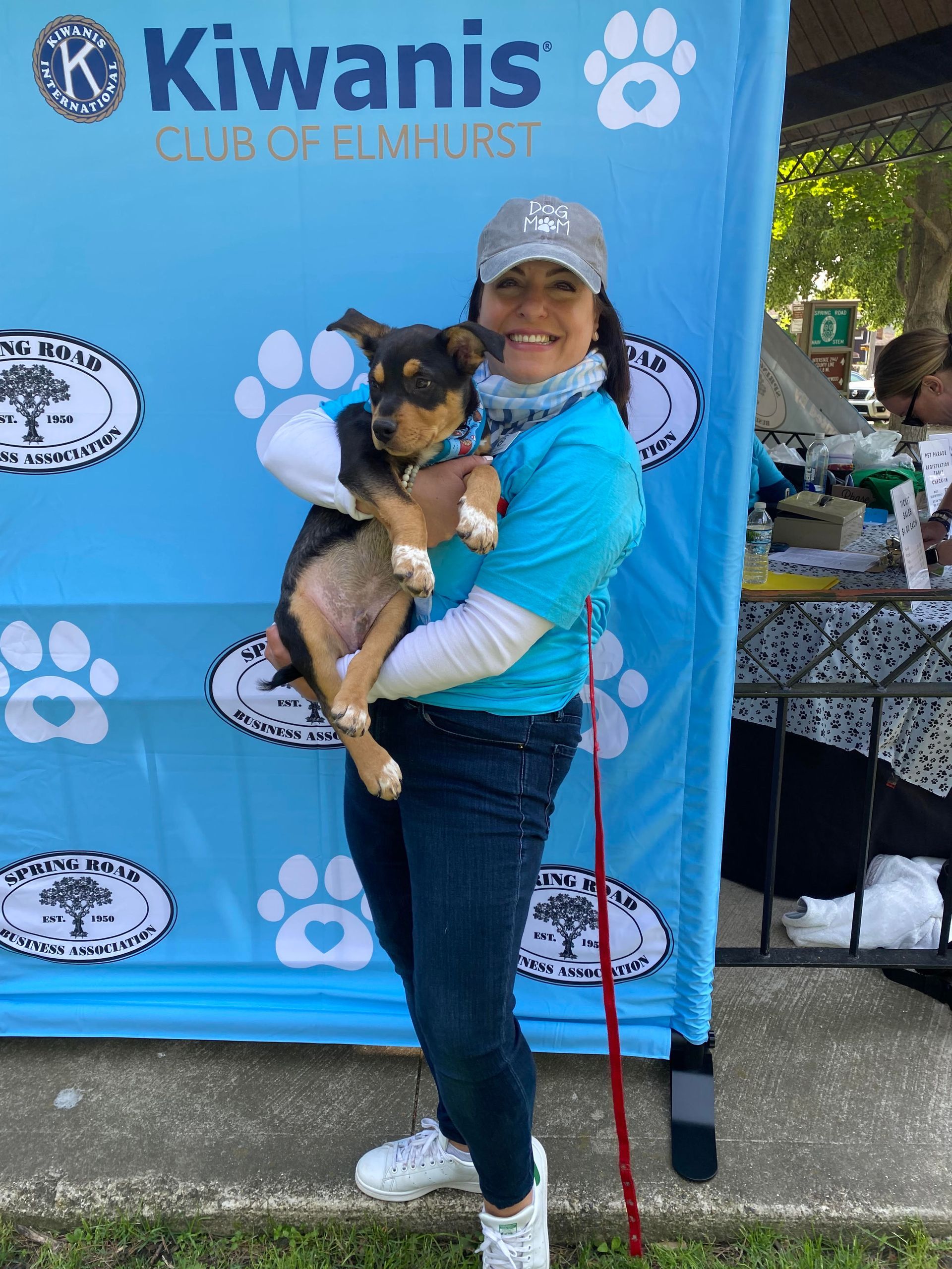 A woman is holding a dog in front of a kiwanis banner