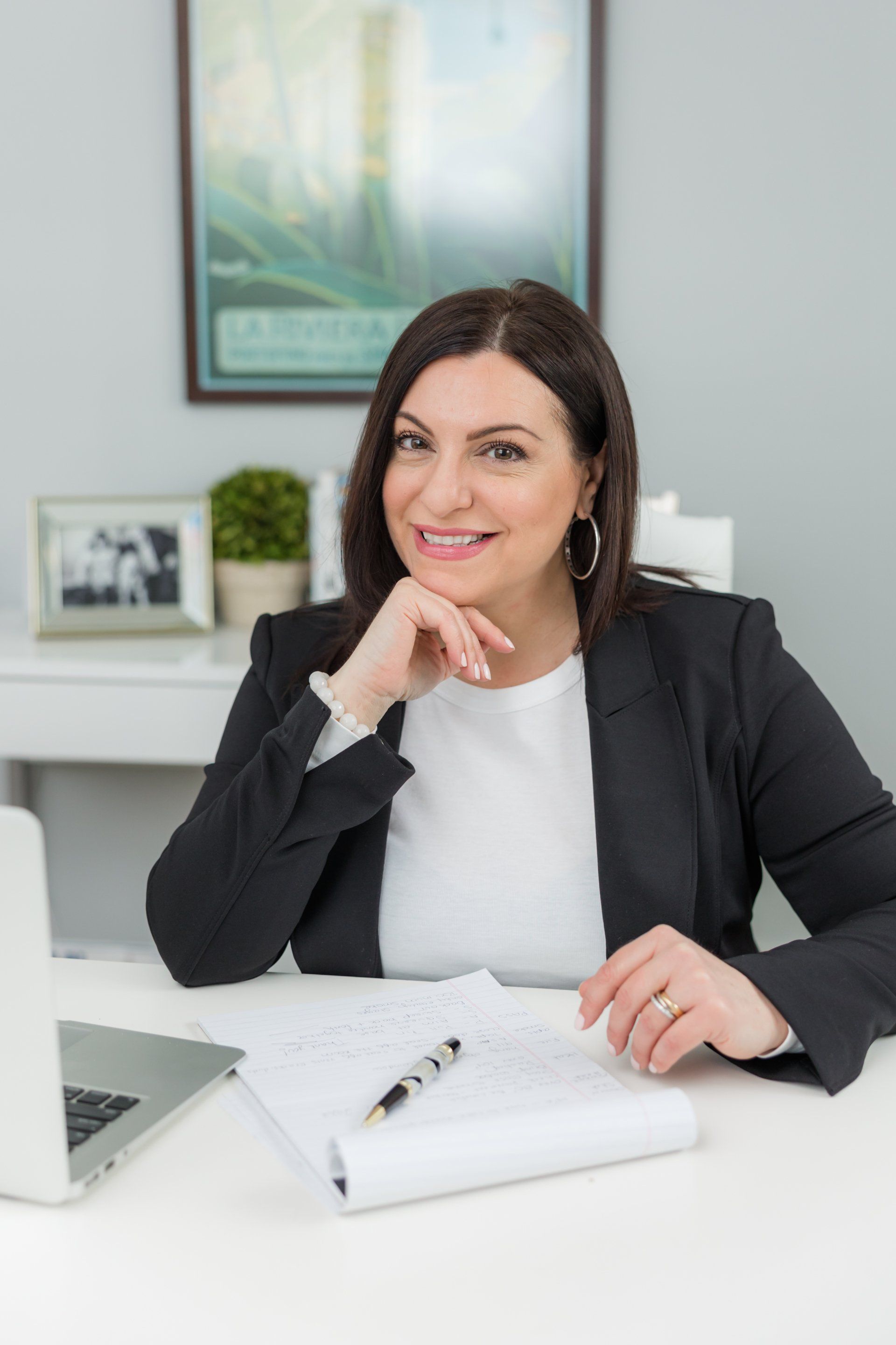 A woman is sitting at a desk with a laptop and a pen.