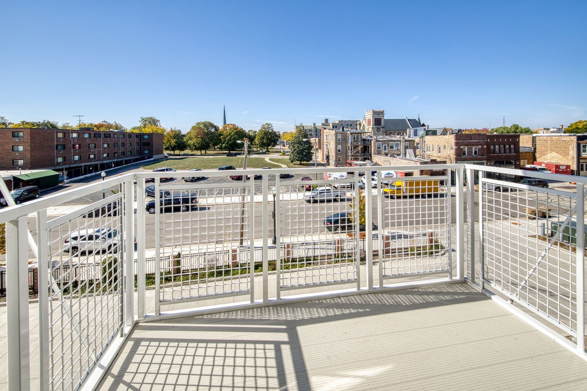 View from a white railing balcony of a city street and buildings on a sunny day.