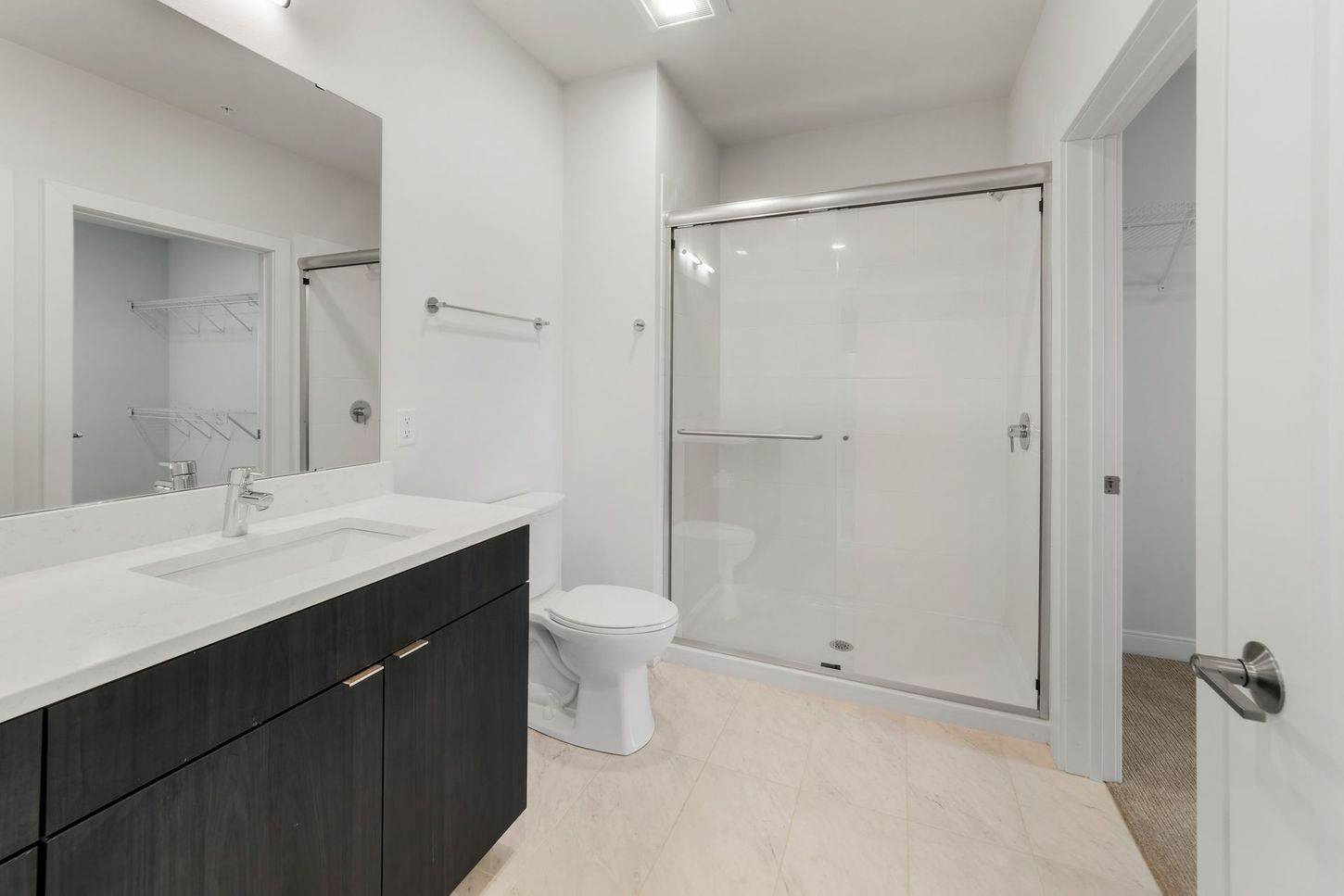 Modern white bathroom with a dark cabinet, glass shower, and toilet.